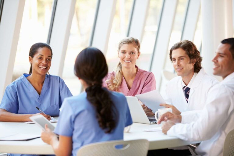 Medical Team Meeting Around Table In Modern Hospital Smiling
