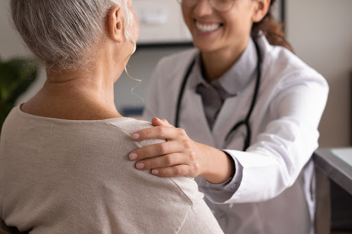 Nurse leader utilizes nonverbal communication by smiling and leaning a hand on patient’s shoulder to invoke trust and comfort- Seyzo, a digital healthcare rounding platform